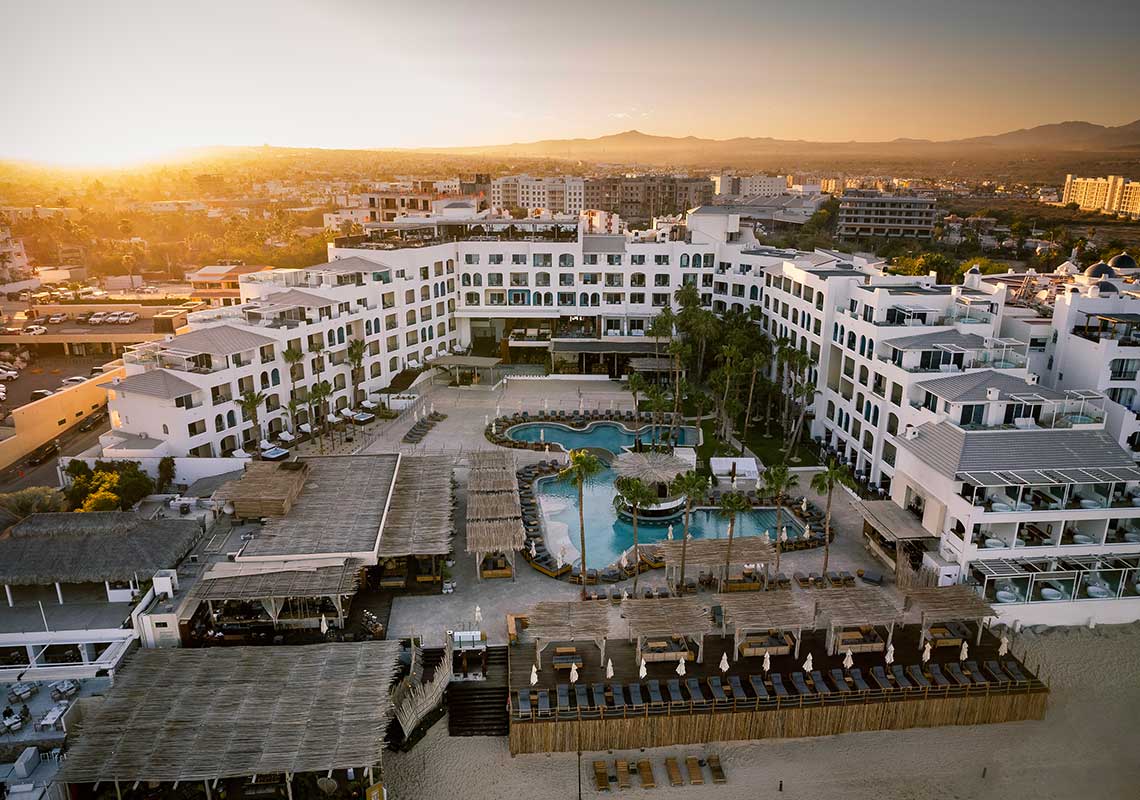 ME Cabo by Melia beachfront resort with lively pool scene and views of Cabo San Lucas coastline, Mexico.