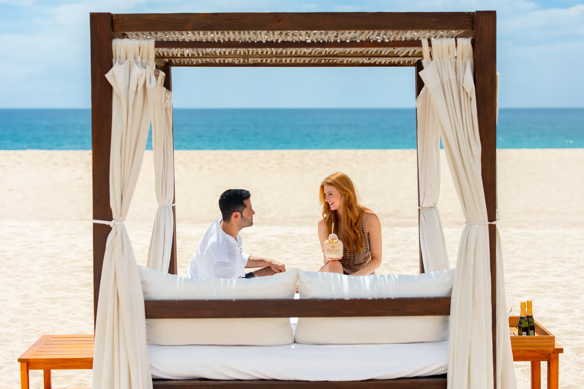 Couple relaxing in a private beach cabana at Zoëtry Casa del Mar Los Cabos enjoying drinks by the ocean.
