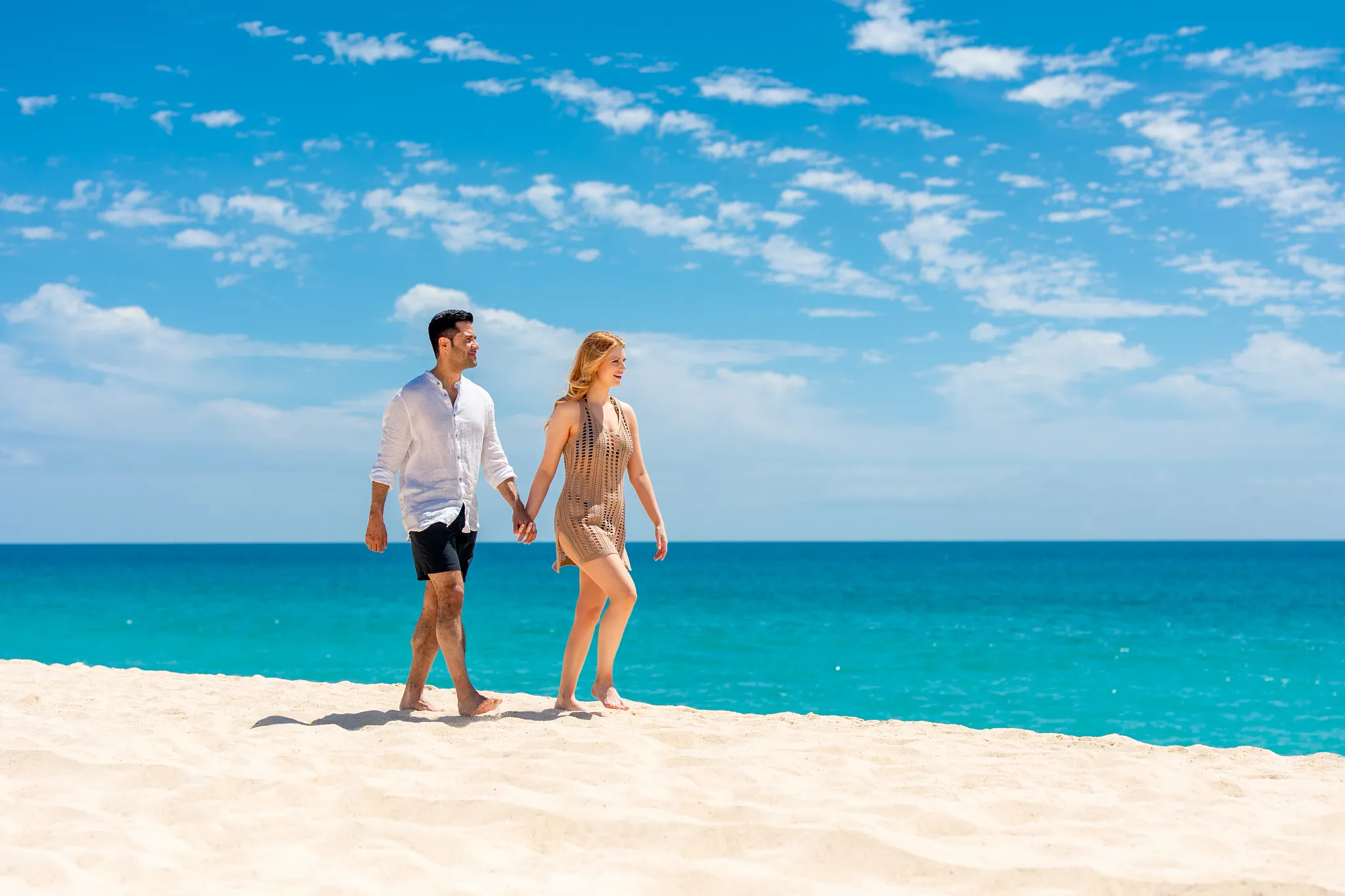 Couple walking hand in hand along sandy beach at Zoëtry Casa del Mar Los Cabos.