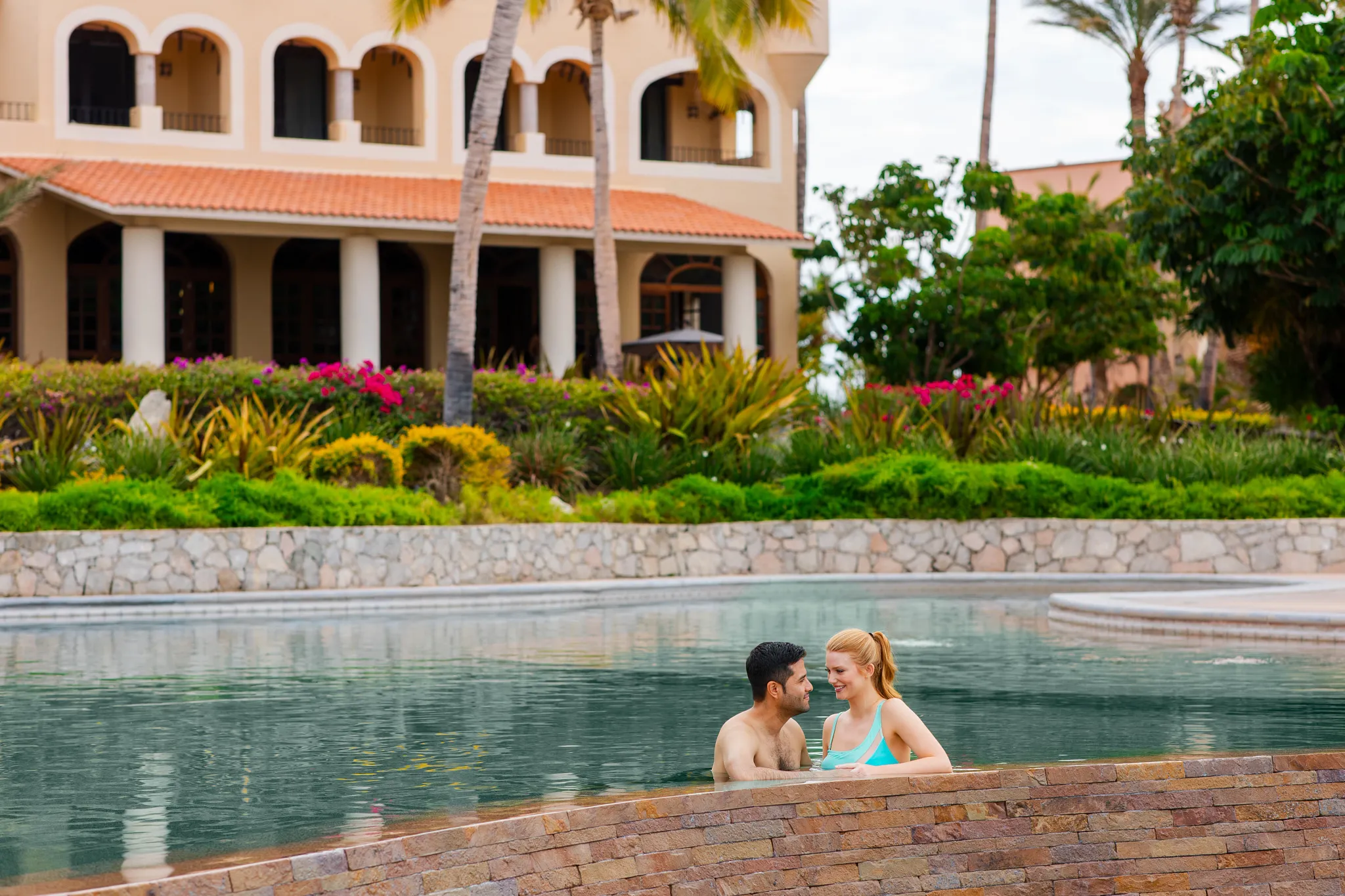 Couple relaxing in an infinity pool at Zoëtry Casa del Mar Los Cabos with lush gardens and resort views.