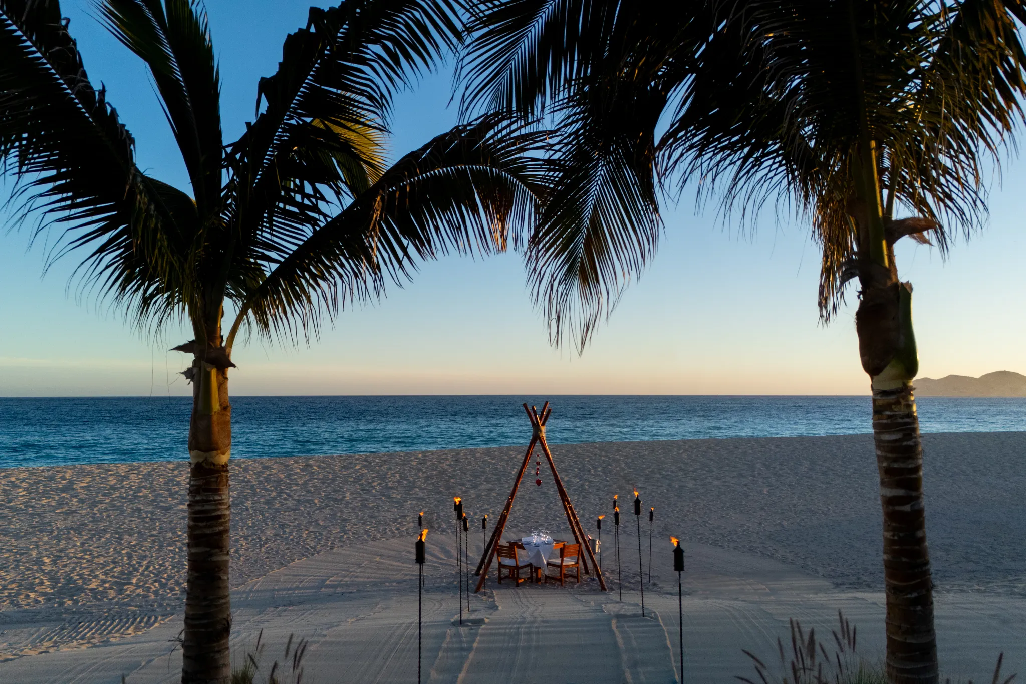 Private candlelit dinner setup on beach at Zoëtry Casa del Mar Los Cabos with torches at sunset.